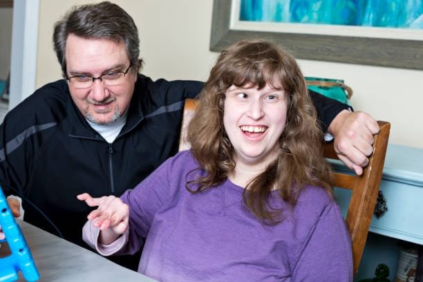 Father assists his autistic daughter with her classwork while using digital tablet at home